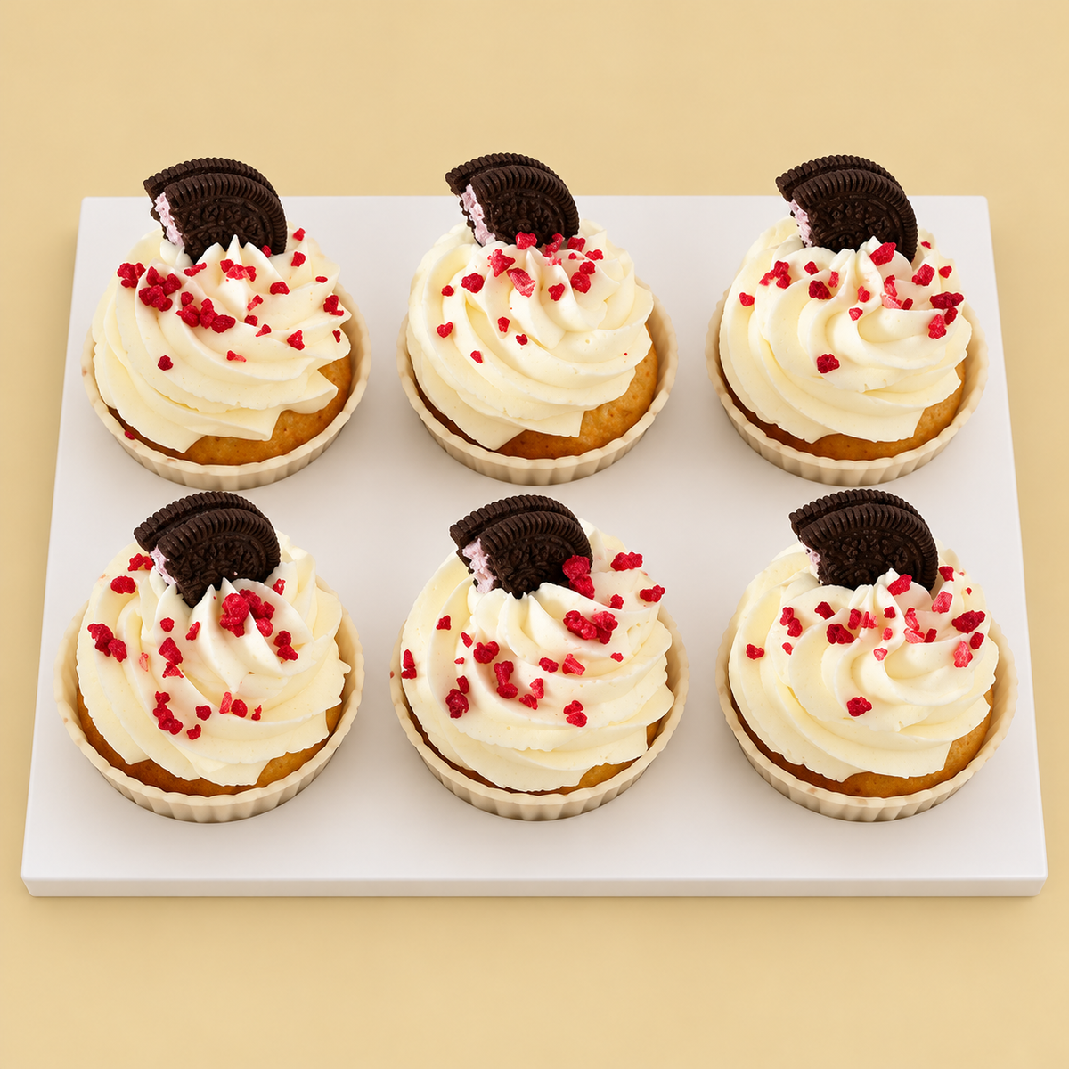 Six cupcakes with ivory cream swirls, chocolate sandwich cookie halves and red crumbs