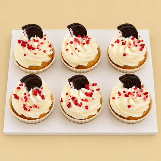Six cupcakes with ivory cream swirls, chocolate sandwich cookie halves and red crumbs